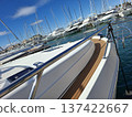 The bow of a sailing yacht with shiny railings. Many yachts are docked in the harbor under a clear blue sky. Masts rise in the background, indicating a busy marina. 137422667