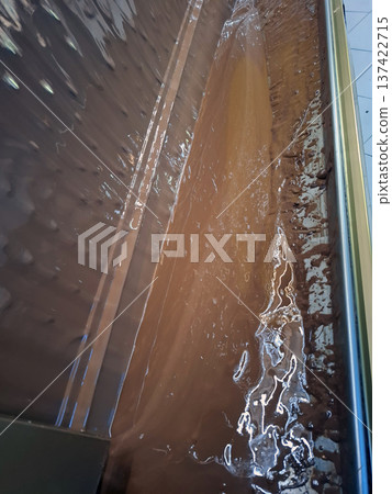Rich melted milk chocolate flows smoothly during a professional tempering process inside a confectionery factory. The shiny surface shows the careful work of chocolatiers. Rich melted milk chocolate flows smoothly during a professional tempering process inside a confectionery factory. The shiny surface shows the careful work of chocolatiers. 137422715