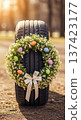 Tire with Easter wreath of flowers and pastel eggs on road outdoors. Spring auto service display, seasonal transport decor, 137423177