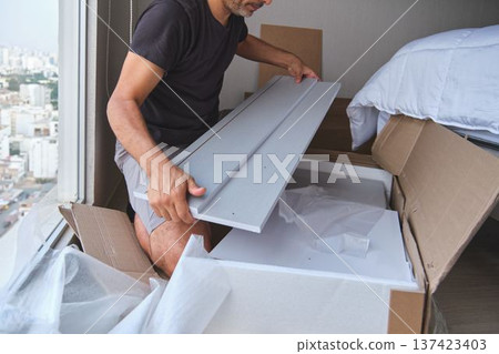 Man assembling flat pack furniture unpacking box home Man assembling flat pack furniture unpacking box home 137423403