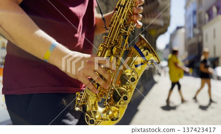 Male fingers of musician play the saxophone on summer day. Natural light reflects off metal surface, highlighting movement and rhythm. Scene captures live urban music and atmosphere street performance Male fingers of musician play the saxophone on summer day. Natural light reflects off metal surface, highlighting movement and rhythm. Scene captures live urban music and atmosphere street performance 137423417