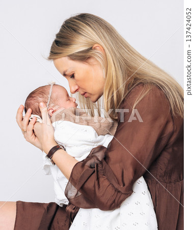 Young mother gently kissing her newborn baby girl. Tender moment of maternal love, care and emotional connection.  137424052