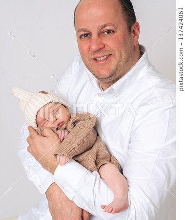 Portrait of a happy father holding his sleeping newborn baby in arms. Concept of fatherhood, parenting and emotional bond between father and child. Portrait of a happy father holding his sleeping newborn baby in arms. Concept of fatherhood, parenting and emotional bond between father and child. 137424061