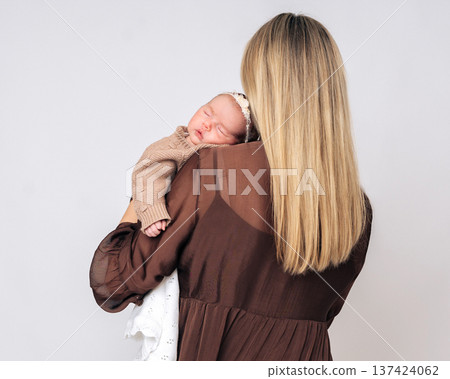 Back view of mother holding sleeping newborn baby on her shoulder. Tender moment of maternal care and emotional connection Back view of mother holding sleeping newborn baby on her shoulder. Tender moment of maternal care and emotional connection 137424062
