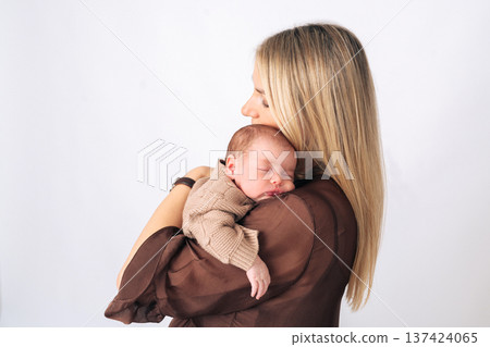 Side view of a mother holding her sleeping newborn baby in arms. Tender motherhood and newborn care concept. Side view of a mother holding her sleeping newborn baby in arms. Tender motherhood and newborn care concept. 137424065