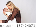 Portrait of caring mother hugging newborn baby girl. Concept of motherhood, parenting, love and family happiness, perfect for Mothers Day themes. 137424071