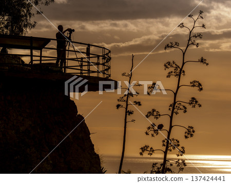 Photographer Silhouette On Cliff Lookout With Tripod Capturing Sunset Over Ocean At Golden Hour Photographer Silhouette On Cliff Lookout With Tripod Capturing Sunset Over Ocean At Golden Hour 137424441