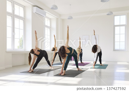 Yoga class performing triangle pose with extended reach and aligned breathing 137427592