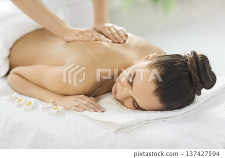 Relaxed young woman lying on massage couch and receiving professional back and shoulder massage. 137427594