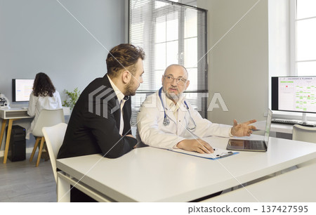 Senior doctor consulting patient in clinic office, discussing results on laptop 137427595