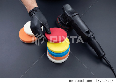 Gloved hand selecting red foam polishing pad near car buffer on dark surface Gloved hand selecting red foam polishing pad near car buffer on dark surface 137427727