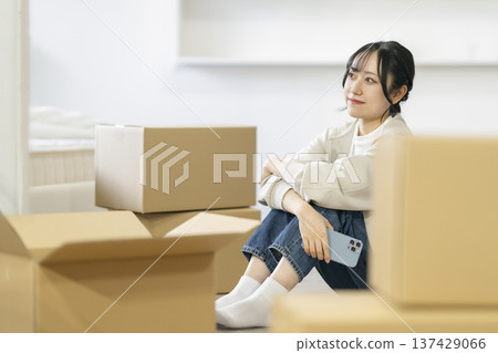 A young woman sitting surrounded by cardboard boxes. Moving image. A young woman sitting surrounded by cardboard boxes. Moving image. 137429066