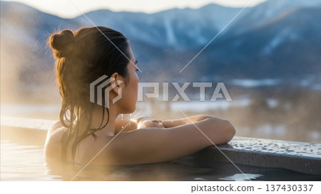 Asian woman relaxing in outdoor hot spring bath with mountain valley landscape during golden hour winter sunset 137430337