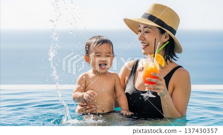 Asian mother and toddler son splashing water together in swimming pool while woman holds tropical cocktail drink during summer vacation 137430357