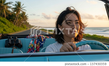 Asian woman driving vintage blue convertible car on tropical coastal highway during golden hour sunset with palm trees and ocean view 137430359