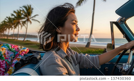 Asian woman driving vintage convertible car during golden hour sunset at tropical beach with palm trees and ocean view 137430360