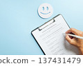 Hand completing customer satisfaction survey form, providing business feedback for review data on clipboard, expressing opinion for quality check, smiley face represents positive experience 137431479