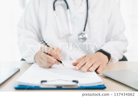Doctor in white coat signs medical form on clipboard at clinic desk with stethoscope and laptop, representing patient consent, healthcare paperwork, insurance claims and consultation. insurance Doctor in white coat signs medical form on clipboard at clinic desk with stethoscope and laptop, representing patient consent, healthcare paperwork, insurance claims and consultation. insurance 137434862
