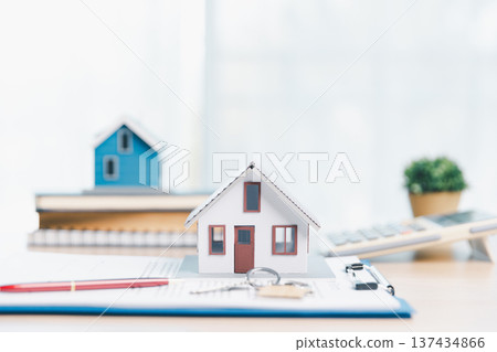 Home buying and mortgage planning concept for real estate investment and insurance, featuring a miniature house, keys, calculator, pen and contract on a bright desk in a modern office. real estate 137434866