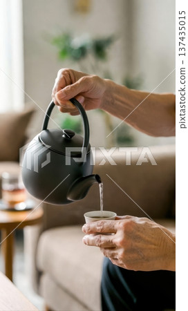 Pouring Tea From Black Teapot Into Cup at Home Pouring Tea From Black Teapot Into Cup at Home 137435015