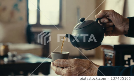 Pouring tea from teapot into cup with elderly hands Pouring tea from teapot into cup with elderly hands 137435165
