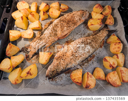 Two fresh fish sea bass baking with potatoes on parchment paper in prague Two fresh fish sea bass baking with potatoes on parchment paper in prague 137435569