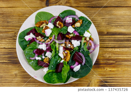 Tasty spinach salad with boiled beetroot, feta cheese, walnut and red onion on wooden table. Top view. Healthy vegetarian food 137435726