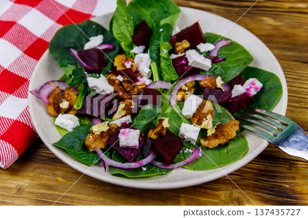 Tasty spinach salad with boiled beetroot, feta cheese, walnut and red onion on wooden table. Healthy vegetarian food Tasty spinach salad with boiled beetroot, feta cheese, walnut and red onion on wooden table. Healthy vegetarian food 137435727