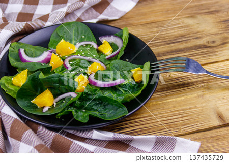 Tasty salad with spinach, orange, red onion and sesame seeds on wooden table. Healthy food or vegetarian concept Tasty salad with spinach, orange, red onion and sesame seeds on wooden table. Healthy food or vegetarian concept 137435729