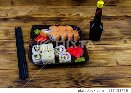 Set of sushi rolls in plastic boxes, soy sauce and chopsticks on wooden table. Sushi for take away or delivery of sushi in plastic containers Set of sushi rolls in plastic boxes, soy sauce and chopsticks on wooden table. Sushi for take away or delivery of sushi in plastic containers 137435736