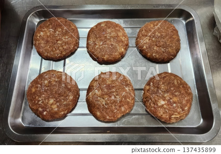 Six Fresh Raw Meat Patties Ready for Grilling on a Metal Tray in a Commercial Kitchen 137435899