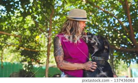 Tattooed woman wearing hat bonding with dog in sunny park 137436068