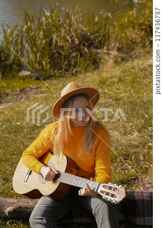 Portrait of smiling caucasian artist plays wooden acoustic guitar in autumnal park. Young songwriter plays string musical instrument hobby outside in nature fall time. Audio music healing 137436787
