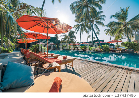 Luxury tropical beach resort swimming pool leisure beds chairs umbrellas palm trees glowing sun rays relaxing summer vacation paradise travel destination 137437490