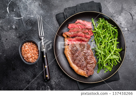 Appetizing grilled striploin steak with salad, inviting you to indulge in a mouthwatering culinary experience. black background. top view 137438266