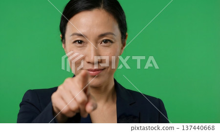 A professional Asian woman points directly at the camera against a green screen, suggesting direction or choice. A professional Asian woman points directly at the camera against a green screen, suggesting direction or choice. 137440668