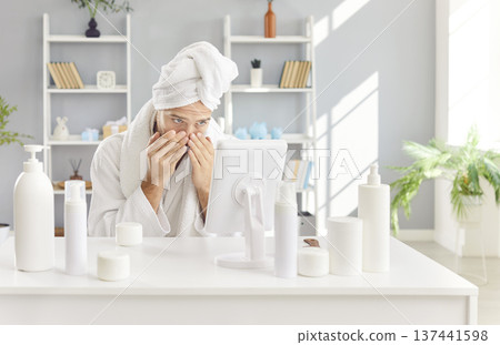 Man in home spa takes care of his skin, looking at reflection in mirror among cosmetic products. Man in home spa takes care of his skin, looking at reflection in mirror among cosmetic products. 137441598