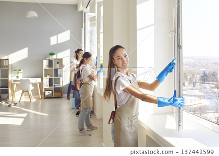 Team of a young janitors cleaning windows in office or at home and looking cheerful at camera. Team of a young janitors cleaning windows in office or at home and looking cheerful at camera. 137441599