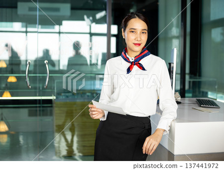 Professional airline staff standing at front counter holding boarding pass in modern lobby. Friendly hospitality staff providing customer service, check in support and guest assistance Professional airline staff standing at front counter holding boarding pass in modern lobby. Friendly hospitality staff providing customer service, check in support and guest assistance 137441972