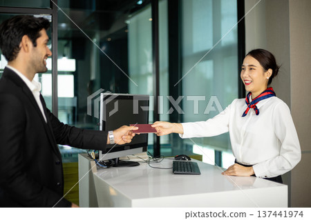 Airline female staff handing passport to passenger at counter during check in process. Friendly hospitality staff providing customer service and welcoming traveler Airline female staff handing passport to passenger at counter during check in process. Friendly hospitality staff providing customer service and welcoming traveler 137441974