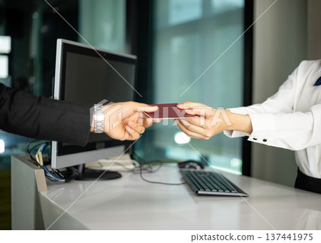 Airline staff receiving passport from passenger during check in at counter. Close up of hospitality service interaction between traveler and staff Airline staff receiving passport from passenger during check in at counter. Close up of hospitality service interaction between traveler and staff 137441975