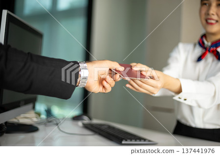 Airline female staff receiving passport from passenger at front desk during check in process. Close up hospitality service interaction Airline female staff receiving passport from passenger at front desk during check in process. Close up hospitality service interaction 137441976