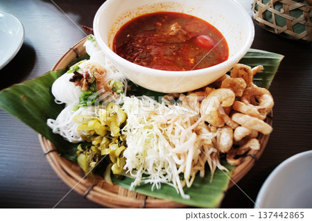Tradition set of Northern Thai cuisine is spicy curry pork soup served with rice vermicelli and fresh vegetable with pork rind on banana leaf in wicker basket Tradition set of Northern Thai cuisine is spicy curry pork soup served with rice vermicelli and fresh vegetable with pork rind on banana leaf in wicker basket 137442865
