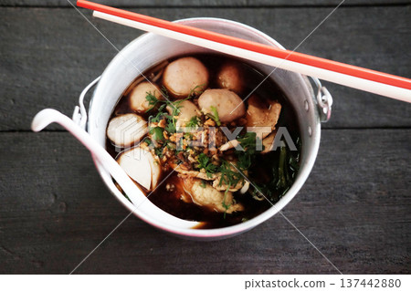Top view of Thai boat noodles with chicken soup and pork balls in aluminum bowl on wooden table 137442880