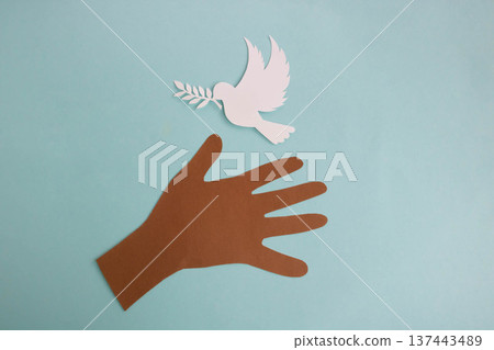 A paper hand reaches out to a paper dove on a blue background. World Peace Day. A paper hand reaches out to a paper dove on a blue background. World Peace Day. 137443489