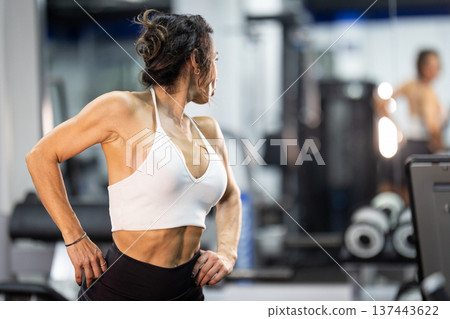 Fit woman showing muscular back in gym environment Fit woman showing muscular back in gym environment 137443622