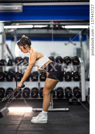 Woman training arm strength with cable machine in gym 137443727