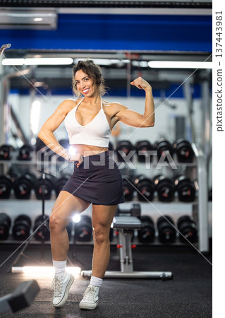 Confident woman flexing biceps showing strength in gym 137443981