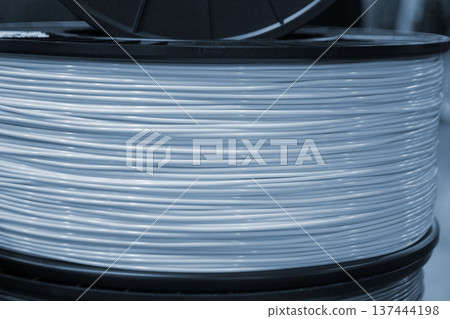 Spool of plastic wire for 3D printing. Spool with white plastic close-up. Component for 3d printing. Printing accessories. Concept modern 3D printing technology. Additive progressive FDM technologies Spool of plastic wire for 3D printing. Spool with white plastic close-up. Component for 3d printing. Printing accessories. Concept modern 3D printing technology. Additive progressive FDM technologies 137444198