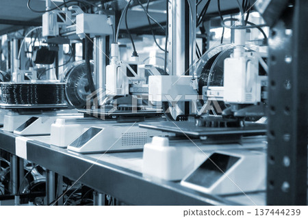 3D printer close up. Working 3D printer in process of printing object from molten black plastic. 3D printer creating model by flowing liquid plastic from extruder of printer. 3D printing technology 137444239